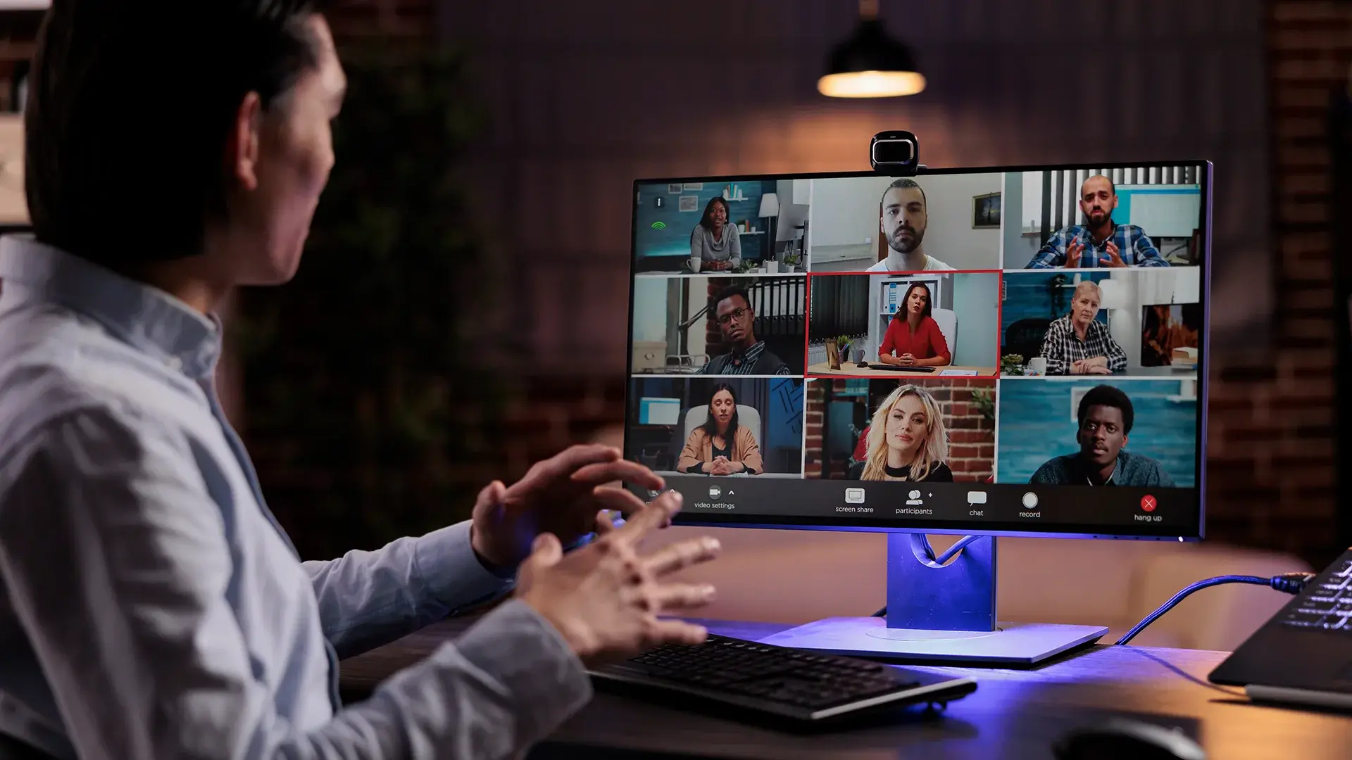 Person participating in a video conference with multiple attendees displayed on a computer monitor.