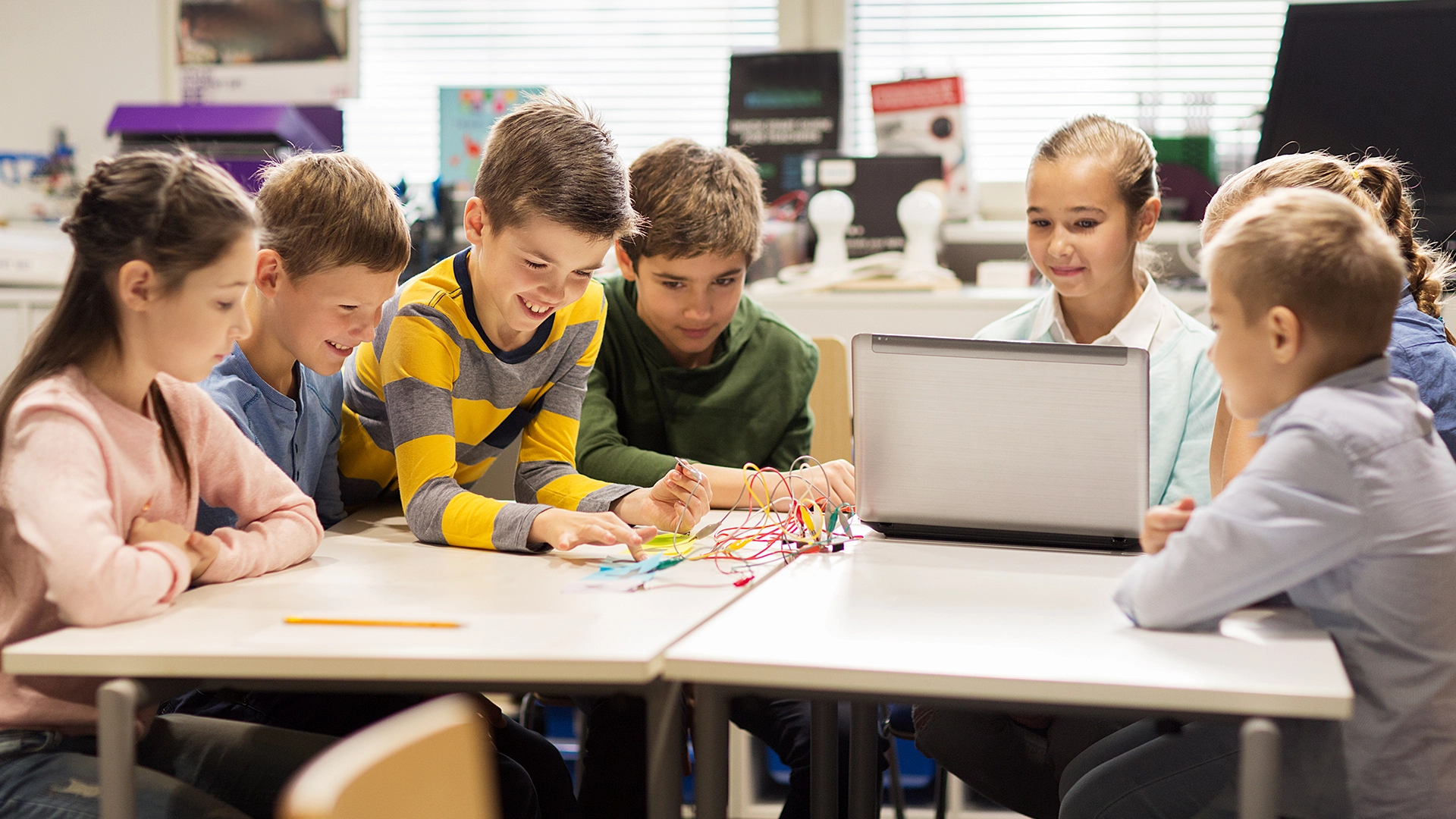 A group of children participates in an eKidsPower-Up session, collaborating on a hands-on STEM project with a laptop and electronics, engaged and excited in a learning environment