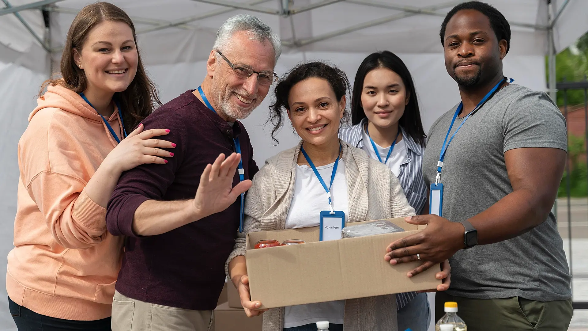 Group of diverse volunteers smiling and holding a box of donated goods, representing community support and assistance efforts associated with ApoyOnline