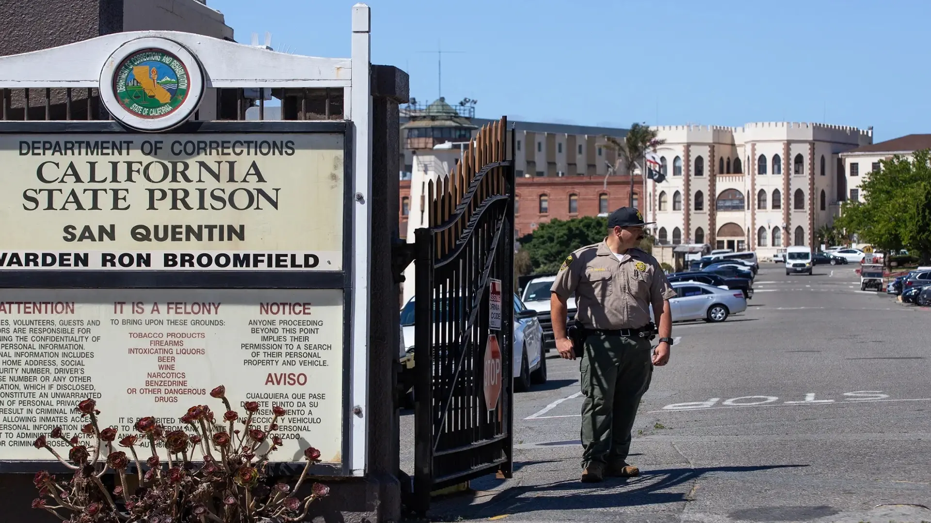 Entrance to California State Prison, San Quentin, with a Department of Corrections sign and a guard standing by the gate, illustrating the facility's security measures