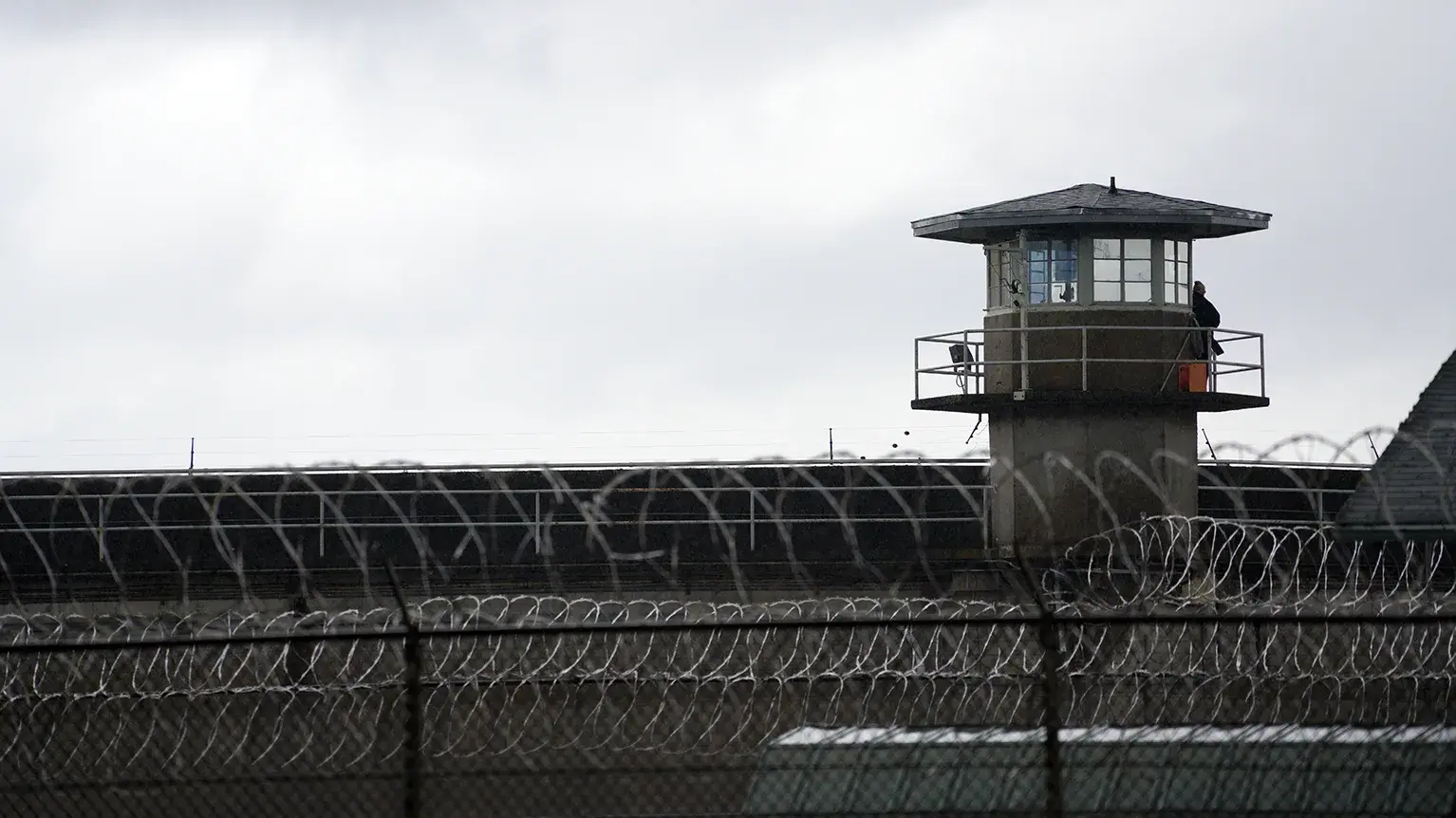 Entrance to California State Prison, San Quentin, with a Department of Corrections sign and a guard standing by the gate, illustrating the facility's security measures