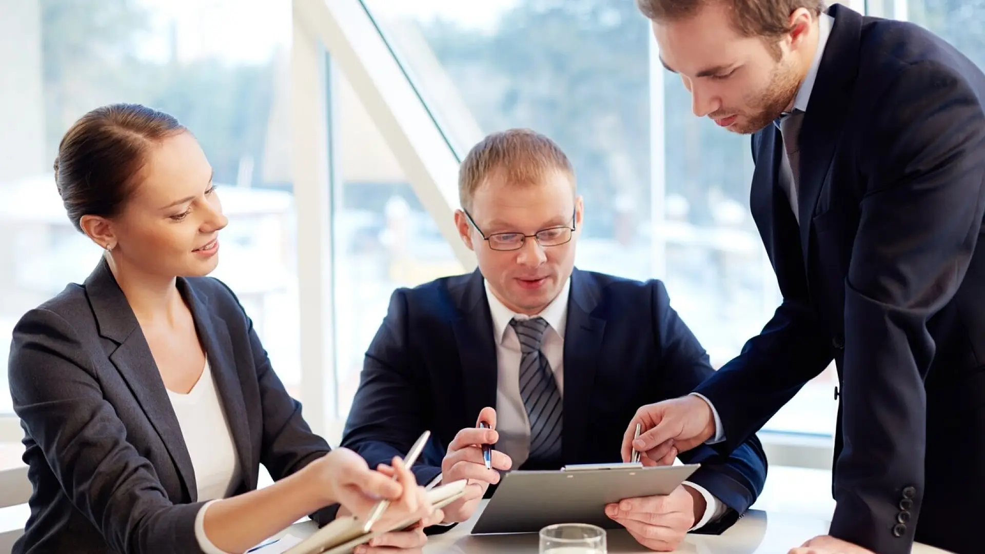 Team of business professionals engaged in a focused discussion, reviewing documents and digital tablets, representing Capita’s dedication to providing consulting, digital services, and professional support solutions