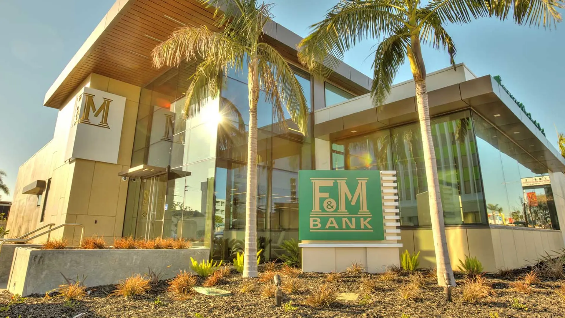 Exterior of Farmers and Merchants Bank building, featuring a modern architectural design with glass walls, palm trees, and a prominent F&M Bank sign, embodying the bank’s commitment to stability and community presence