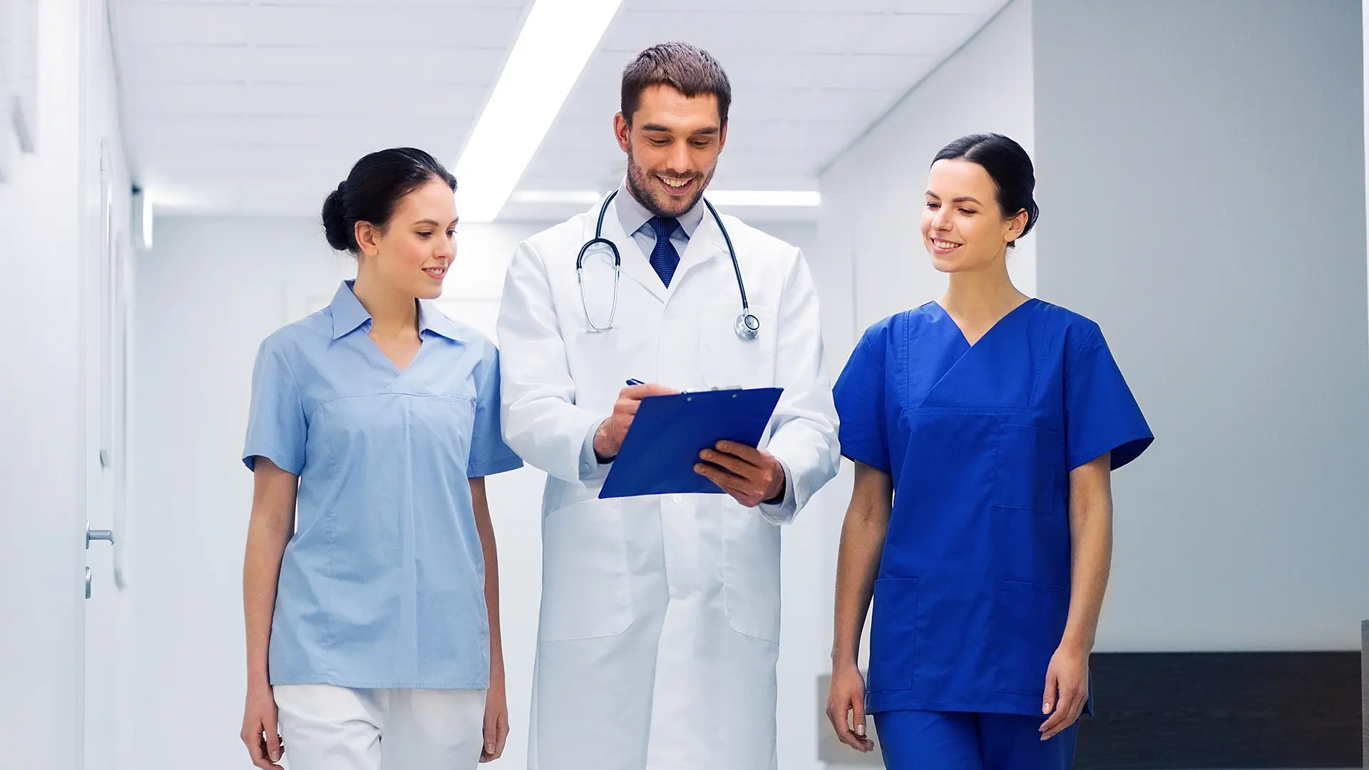 A doctor and two healthcare professionals review a chart together in a hospital corridor, representing VIDIZMO’s support for secure video solutions in healthcare for training, collaboration, and patient care