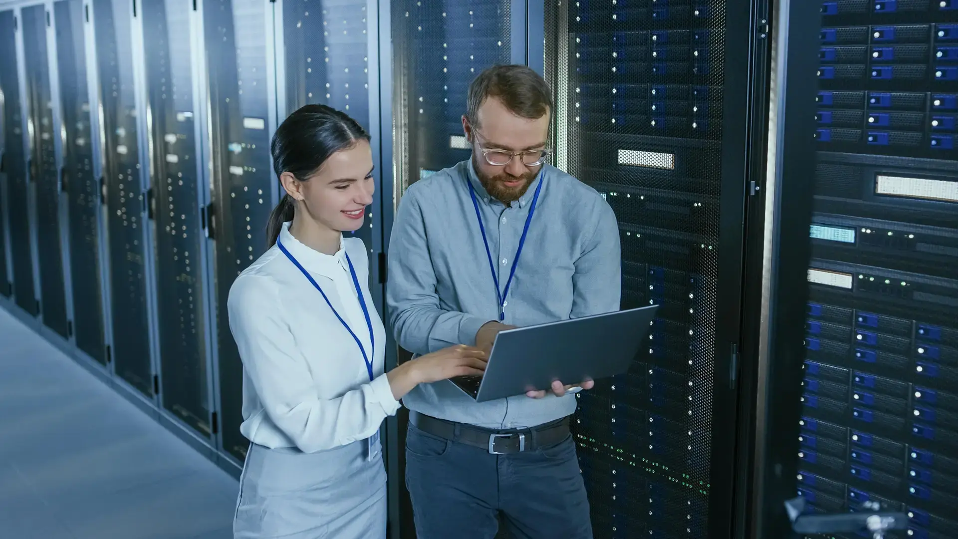 Two colleagues with a laptop standing between server racks in an enterprise data center.