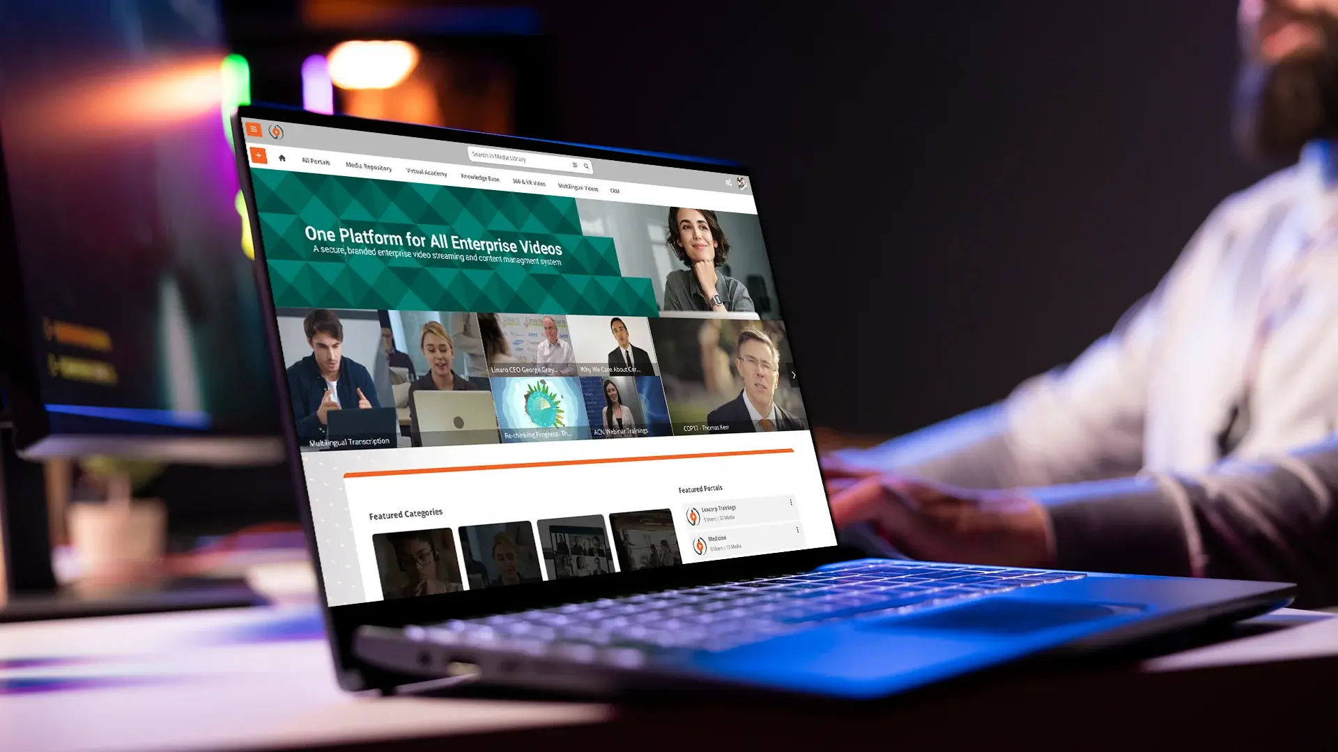 Laptop displaying a business video streaming platform dashboard while a person works in the background.
