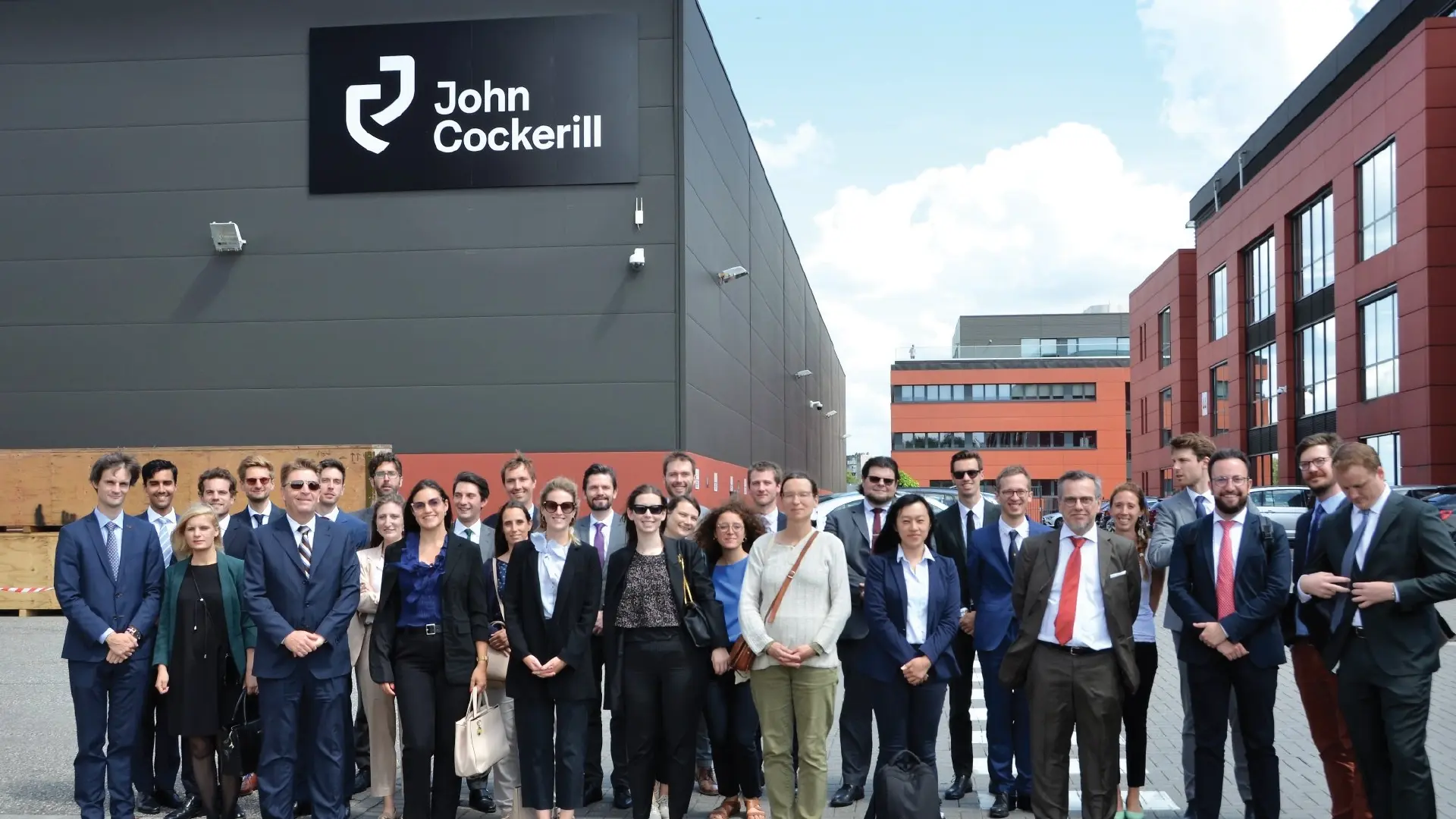 A group of professionals stands outside the John Cockerill facility, highlighting a corporate visit or business gathering at the company’s premises