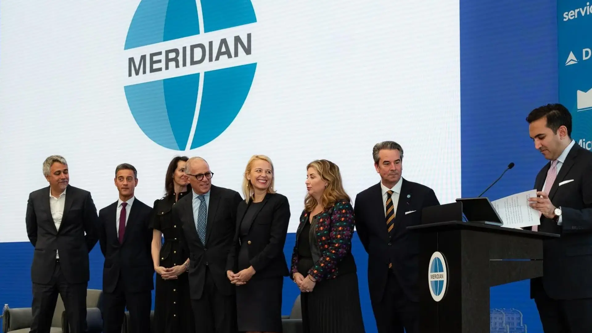 Group of professionals standing on stage at a Meridian International Center event, with the Meridian logo displayed on a large screen in the background, symbolizing global leadership and diplomatic exchange initiatives