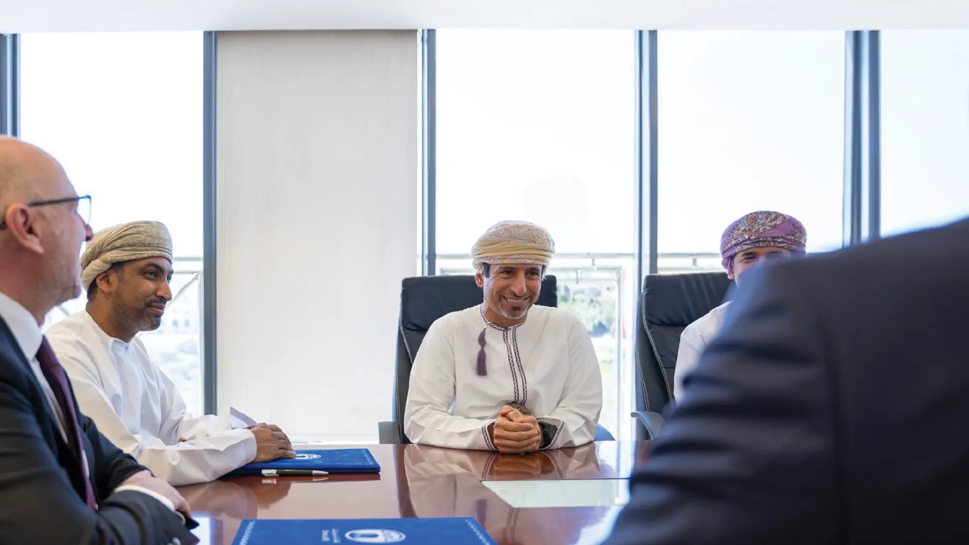 A group of executives, including Omani representatives in traditional attire, sit around a conference table, symbolizing a business meeting related to Oman LNG’s energy initiatives