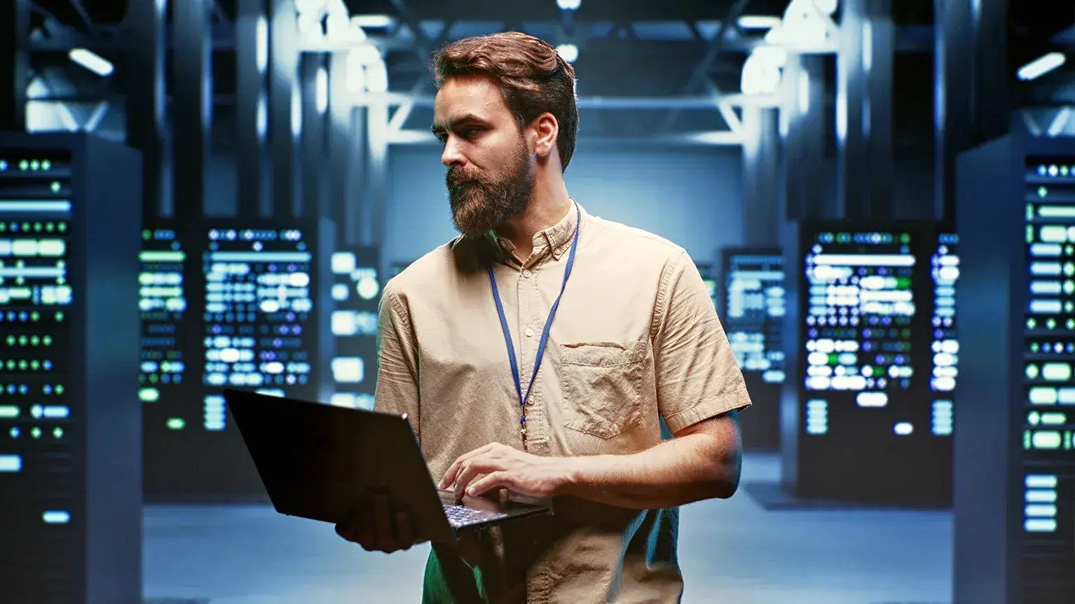 A person holding a laptop and walking through a room of servers.