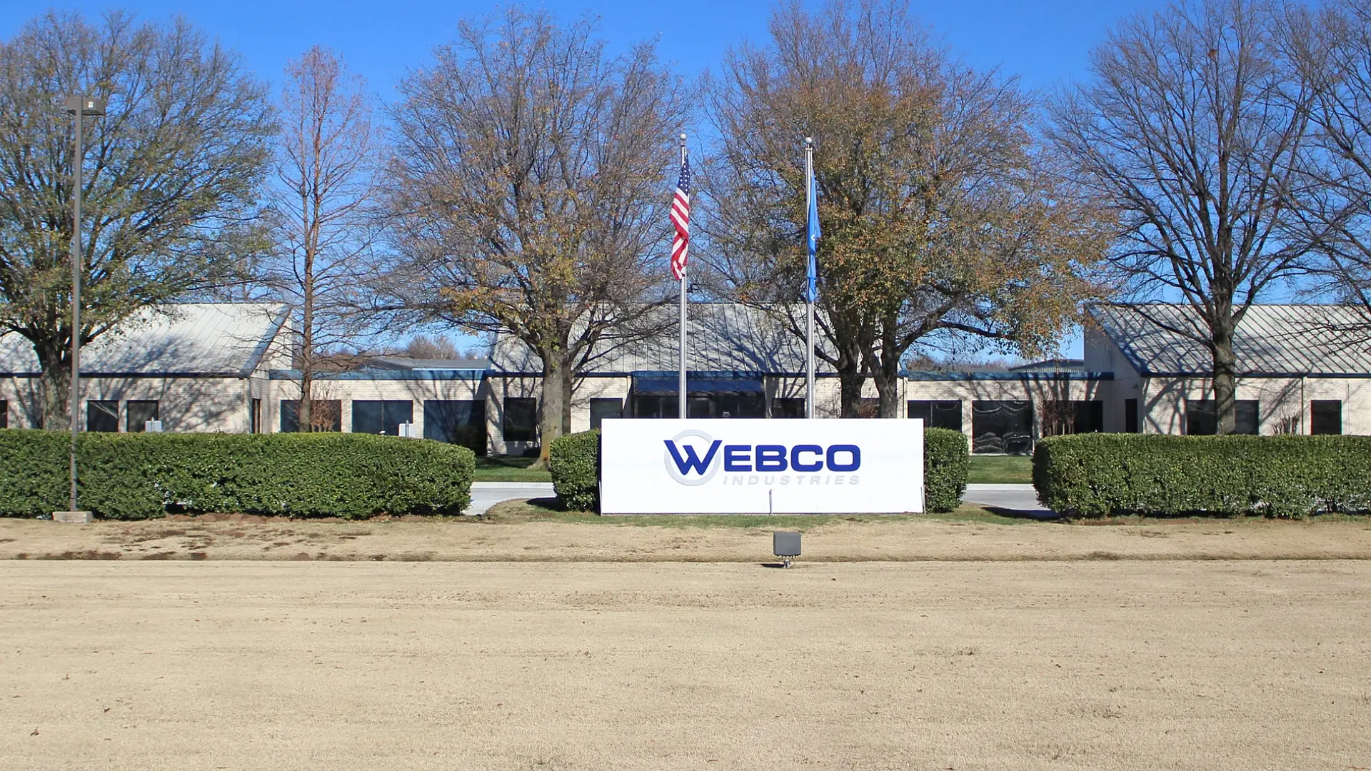 Exterior view of Webco Industries facility with a large company sign and American flag, representing its role in manufacturing and industry