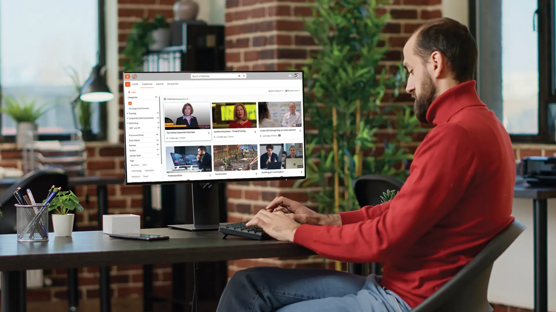 Man working at a desk using a computer to manage and watch webcasting or enterprise video content on screen.
